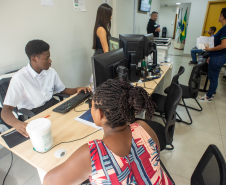 Atendimento ao público no interior da Defensoria, com servidores auxiliando cidadãos em balcões de recepção, em um ambiente iluminado e organizado.