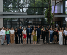 Autoridades e servidores da Defensoria Pública posam para foto na frente do prédio, vestindo trajes formais. Alguns seguram documentos e faixas comemorativas.