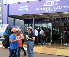 Imagem colorida horizontal em plano aberto em que se vê duas moças recebendo um panfleto de uma moça com informações sobre os serviços da DPE-PR durante o evento Assembleia Itinerante realizado em Londrina.