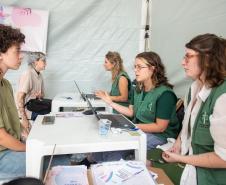 Servidores de colete verde da Defensoria realizam mutirão em tenda montada na rua. 