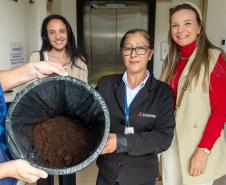 Três mulheres posam com a borra de café na sede da Defensoria. Toda borra do café passado na instituição será entregue no Ecoponto da Prefeitura de Curitiba onde vira adubo em um minhocário.   