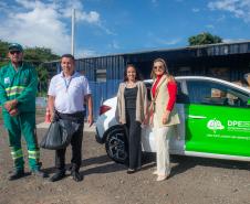 Quatro pessoas em frente a um carro da DPE-PR fazem a entrega da borra de café no Ecoponto da Prefeitura de Curitiba. 
