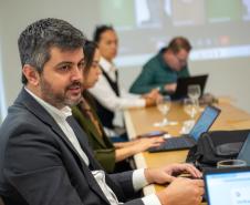 Em primeiro plano se vê homem de cabelo levemente grisalho e terno e ao fundos outras duas pessoas 