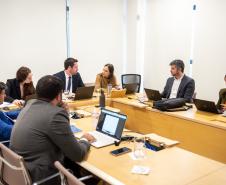 Imagem mostra um grupo de sete pessoas sentadas a mesa com laptops.