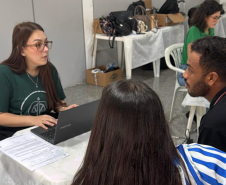 Imagem mostra servidora da DPE-PR realizando atendimento de um casal. A mulher está de costas em primeiro plano e ao fundo homem fala com a servidora. 