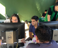 Imagem mostra três servidores utilizando computadores durante os atendimentos do mutirão. De costas em primeiro plano se vê um assistido.