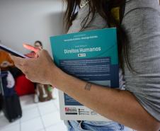 Imagem mostra o braço de uma mulher em close segurando livro jurídico para consulta antes da prova do V Concurso Público para Defensora e Defensor Público do Estado do Paraná. 