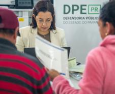 Assistidos aparecem de costas desfocados entregando documentos à servidora da DPE-PR em Mutirãop de Conciliação. 
