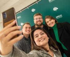 Servidor empossado hoje posa para selfie com a família em frente a backdrop da Defensoria. 