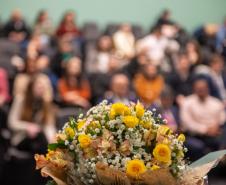 Em primeiro plano flores e ao fundo auditório lotado com familiares dos novos servidores.