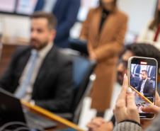 Imagem de celular em primeiro plano com a reunião ao fundo desfocada. 