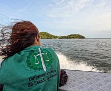 Defensor Público de costas usando colete da instituição está em um barco indo em direção à Guaraqueçaba. 