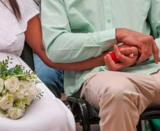 Detalhe das mãos dos noivos entrelaçadas. A noiva segura um buquê de flores.