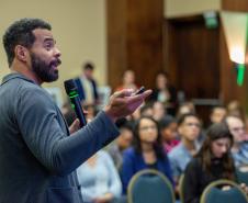 Homem negro em primeiro plano fala para uma plateia ao fundo desfocada. Palestra com especialista do Google sobre uso da Inteligência Artificial.