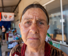 Imagem com o rosto de uma senhora olhando diretamente para a câmera que a fotografou. Ela esta séria e não demonstra nenhuma expressão.