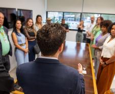Marcel Jeronymo Lima Oliveira aparece de costas e ao fundo as autoridades e lideranças de movimentos sociais durante a posse como ouvidor-geral da Defensoria Pública do Estado do Paraná.