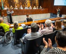 Cadeirante em primeiro plano e público ao redor aplaudem lançamento do NUPED na ALEP.