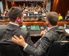 Defensores públicos de costas se cumprimentam na mesa diretora do lançamento do NUPED. Ao fundo o público presente.