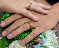 Detalhe das mãos com alianças sobre um buquê de flores. 