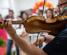 Imagem mostra um violino em primeiro plano e os noivos e noivas ao fundo desfocados.
