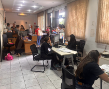 Imagem mostra várias mesas de atendimento com assistidos recebendo orientações dos servidores da Defensoria Pública do Paraná. 