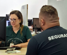 Usuário de costas utilizando uma camiseta com a palavra "segurança" é atendido por uma servidora da Defensoria no Mutirão realizado em Maringá.