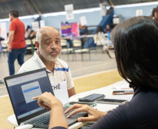 Imagem mostra um homem negro sentado na mesa com servidor que realiza o atendimento durante um Mutirão da Defensoria Pública do Paraná.