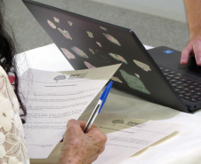Detalhe mostra as mãos de assistida e de servidor da DPE-PR durante atendimento. 