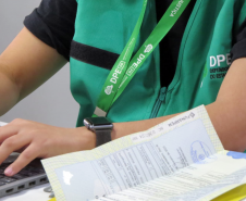 Imagem mostra detalhe de servidora com colete da DPE-PR. 
