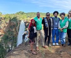 Equipe da Defensoria posa ao lado de indígenas e ao fundo uma cachoeira que fica dentro do território.