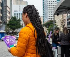 Mulher de costas segura os panfletos com informações sobre violência de gênero e onde procurar apoio.