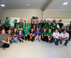 Fotografia de um grande grupo posando sorridente em um salão claro. Muitas pessoas vestem o colete verde da DPE-PR, acompanhadas por outras em trajes casuais. Ao fundo, há letreiros indicando "Centro POP".