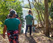 Imagem mostra mulher quilombola e um servidor da DPE-PR, ambos de costas, seguindo por trilha no quilombo.