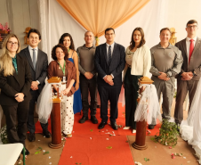 Nove pessoas posam para a foto. Quatro mulheres e cinco homens. Todos trajando roupas formais para os casamentos. 