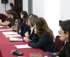 Na imagem vemos os participantes do II Encontro das Equipes Técnicas da DPPR sentados em uma mesa lateral comprida. Todos estão com um tanto virados para a direita, prestando atenção em quem fala. 
