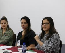 Temos as Assistentes Sociais do CAM Ponta Grossa, Ana Letícia de França e Evelyn Soares,ao fundo, sentadas no lado direito da mesa de falantes e  Taísa de Oliveira ,Assistente Social do CAM Curitiba, na ponta esquerda da mesa. 