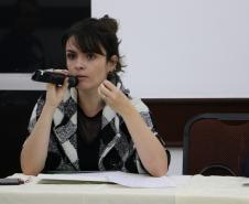 A imagem mostra a Dra. Flávia Palazzi, Diretora da EDEPAR, com um microfone próximo a sua boca sentada na ponta direita da mesa de palestrantes. 