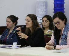 Vemos três participantes do evento. Camylla Basso, sentada centralmente, psicologa da Coordenação de Planejamento aparenta estar realizando uma pergunta.  