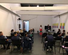 Na imagem vemos a equipe da DPPR palestrando aos guardas municipais. A equipe está de pé, ao fundo da sala, na frente dos oficias (esses estão sentados de costas).