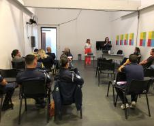 Na imagem vemos a equipe da DPPR palestrando aos guardas municipais. A equipe está de pé, ao fundo da sala, na frente dos oficias (esses estão sentados de costas).