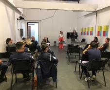 Na imagem vemos a equipe da DPPR palestrando aos guardas municipais. A equipe está de pé, ao fundo da sala, na frente dos oficias (esses estão sentados de costas).