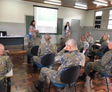 A foto foi tirada no fundo da sala. Nela vemos os soldados sentados em algumas certeiras prestando atenção na equipe da DPPR que está na parte da frente da sala, palestrando, 