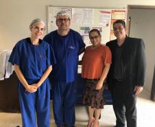 Na imagem vemos a Dra. Eliana Lopes vestindo roupas azuis de cirurgião acompanhada de mais três pessoas. 