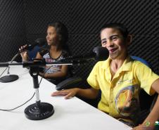 Na imagem vemos duas crianças em um estúdio de rádio, sentadas na mesa de gravação. 