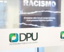A foto foi tirada de uma porta transparente. onde está colada a logo da DPU. Essa se encontra em destaque na imagem. 