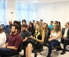 Na imagem vemos o público do evento, estão todos sentados, prestando atenção em algo que lhes é dito/mostrado a sua frente. 