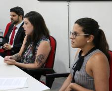Na imagem vemos três pessoas sentadas a uma mesa principal passando informações aos novos defensores. 