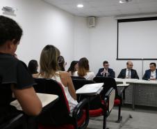 Na imagem vemos uma parte dos novos defensores sentados prestando atenção nos componentes da mesa a sua frente. 