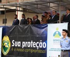 Palanque do evento com convidados na parte de cima da foto. Na parte de baixo, na direita, um aluno do Colégio Militar.  