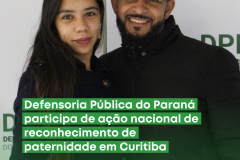 A imagem mostra pai e filha socioafetivos em frente a um painel com o nome e o logotipo da Defensoria. Ambos sorriem para a foto e estão próximos um do outro, em uma posição de proximidade e afeto.
